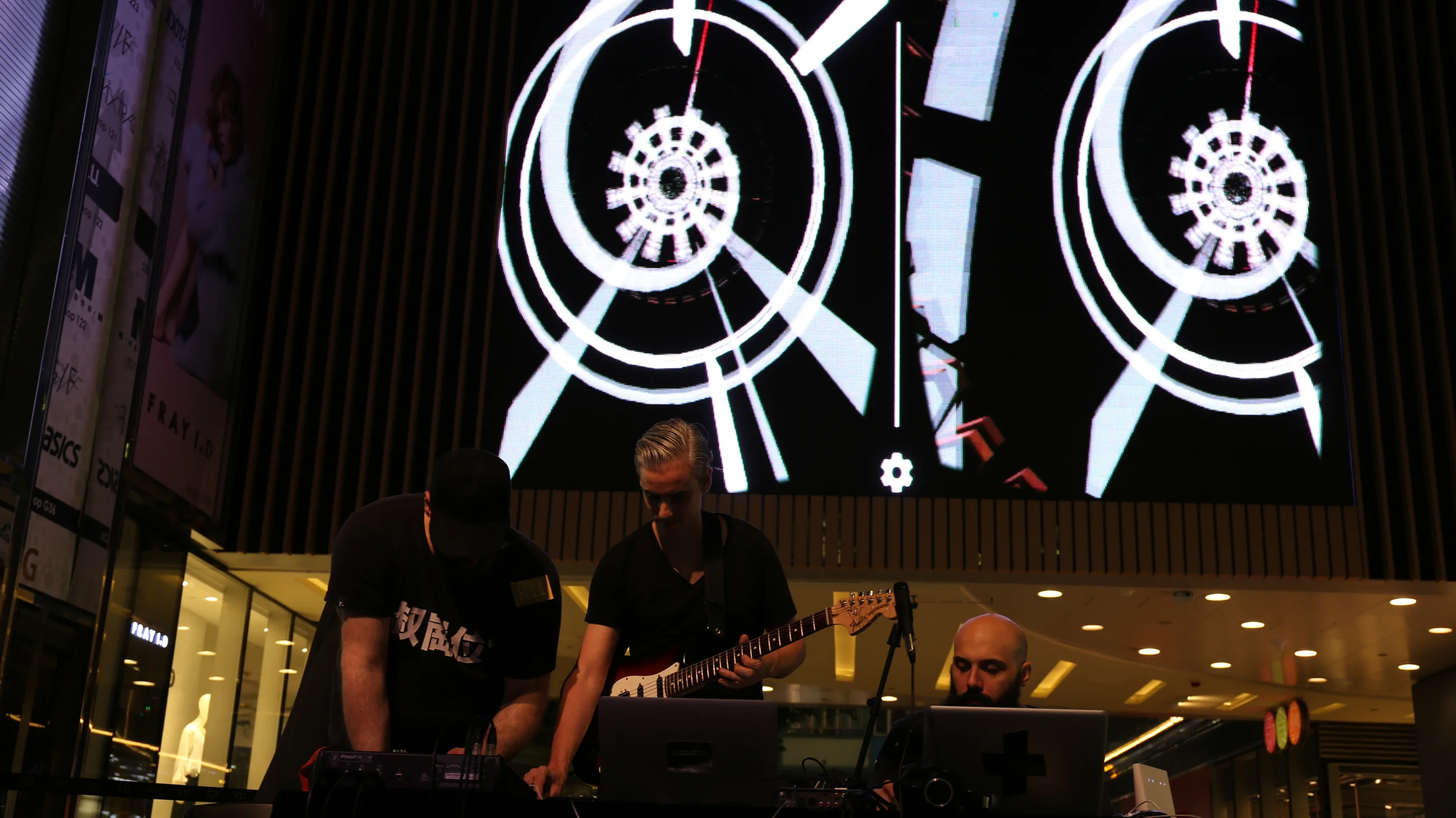 Musicians perform below a large screen displaying circular graphics.