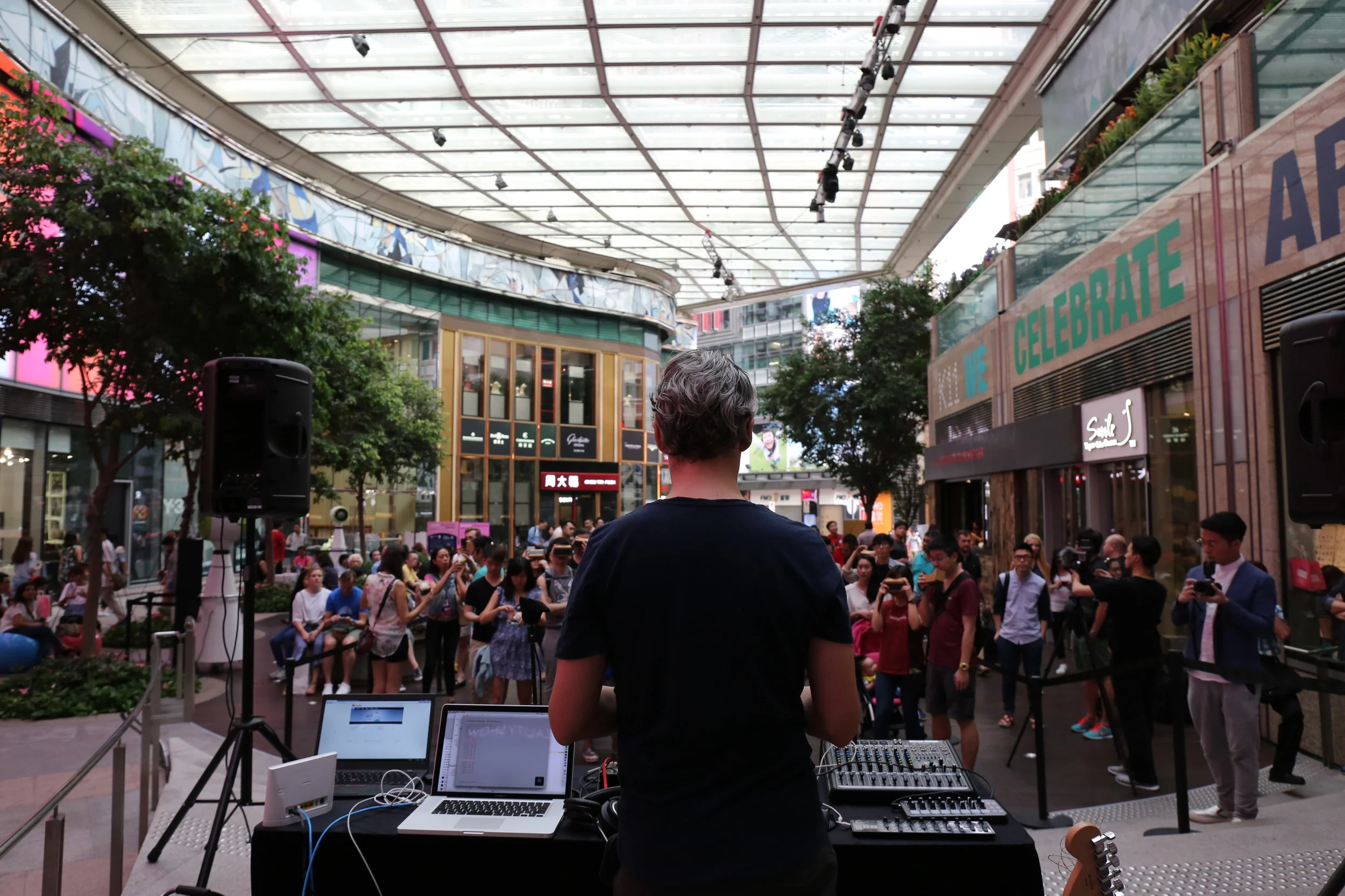 A performer at the mixing desk faces an outdoor audience during Awkward Consequence.