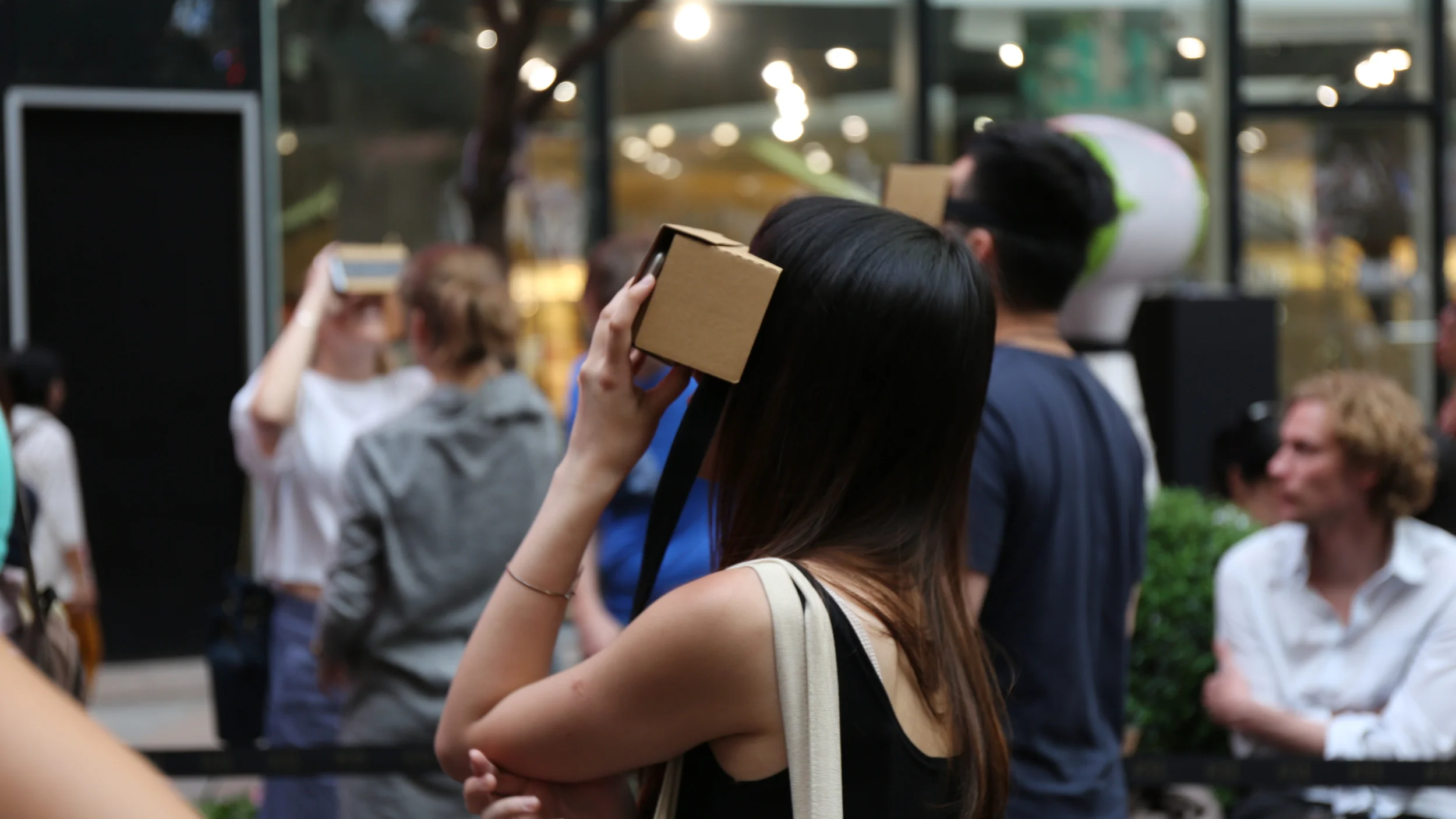 A participant raises a cardboard VR viewer while standing among the audience.