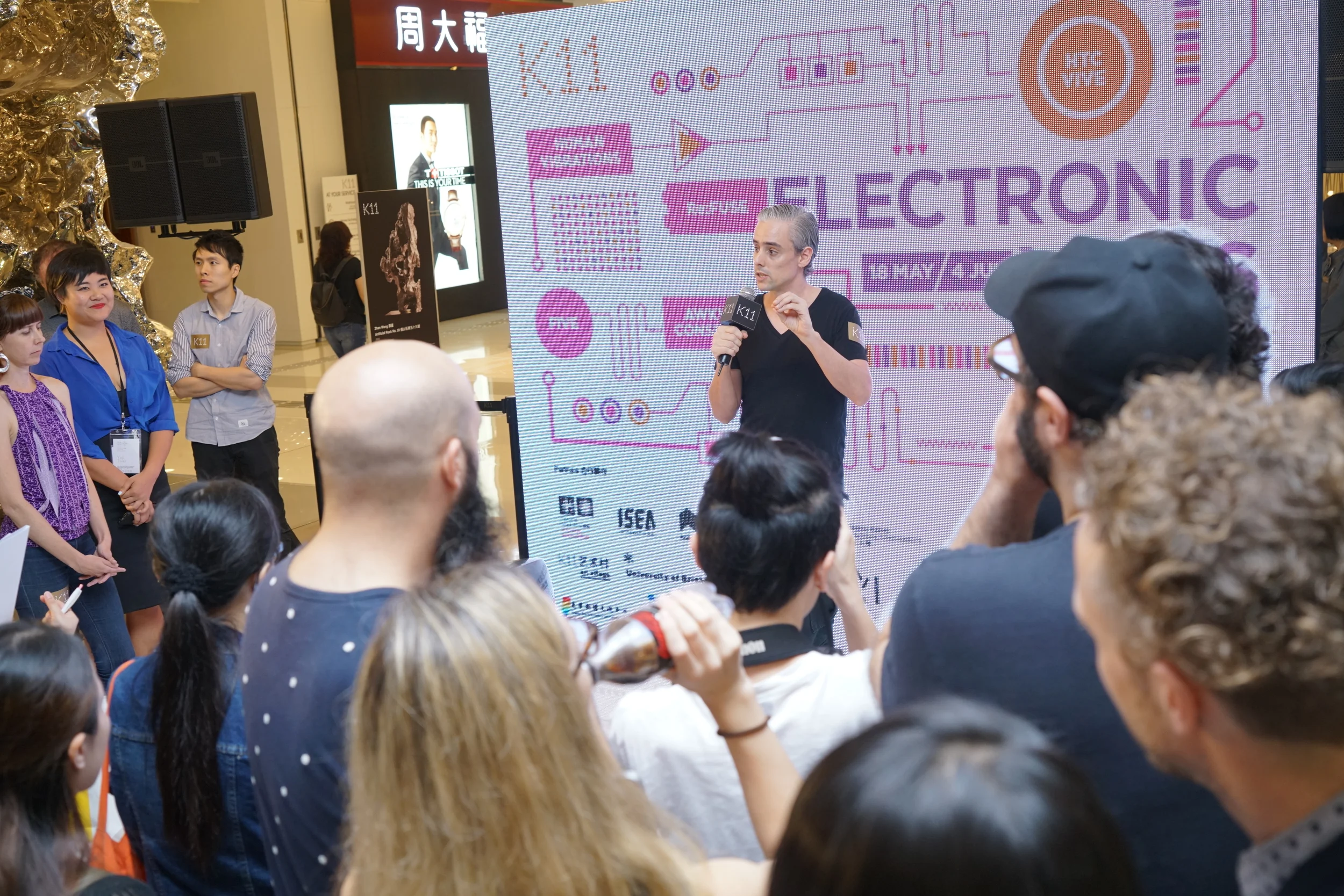 A performer addresses the gathered audience with a microphone.