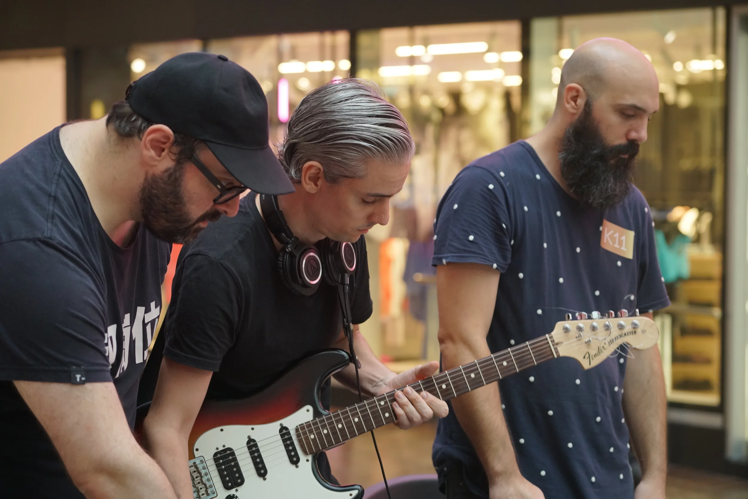 Three performers work at a laptop and electric guitar.