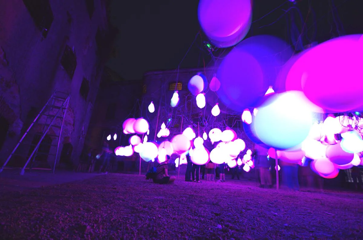 Celebra installed outdoors at night, with illuminated balloons beside a building.
