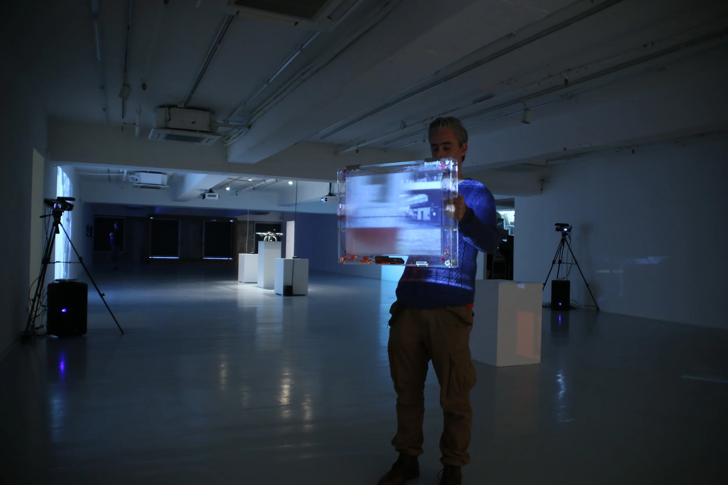 A participant holds an illuminated handheld screen in the darkened Foreign Helpers installation.
