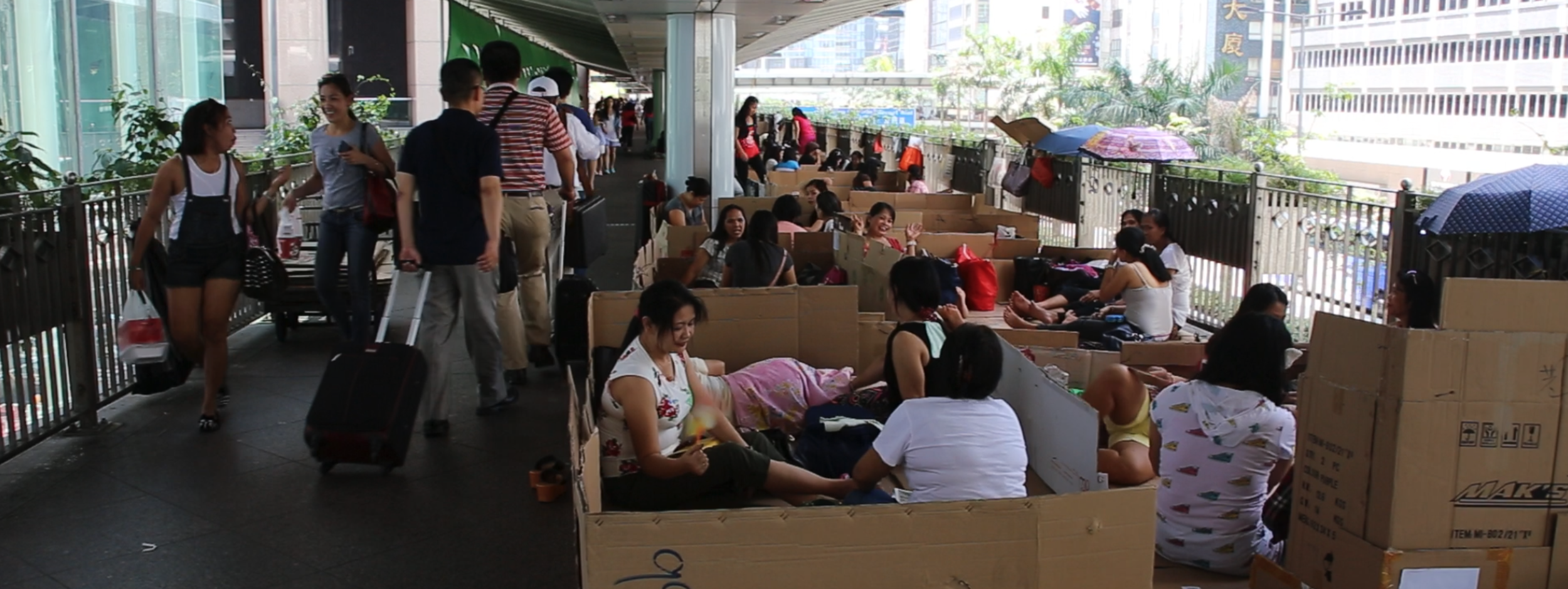 People sitting on cardboard along a covered walkway.