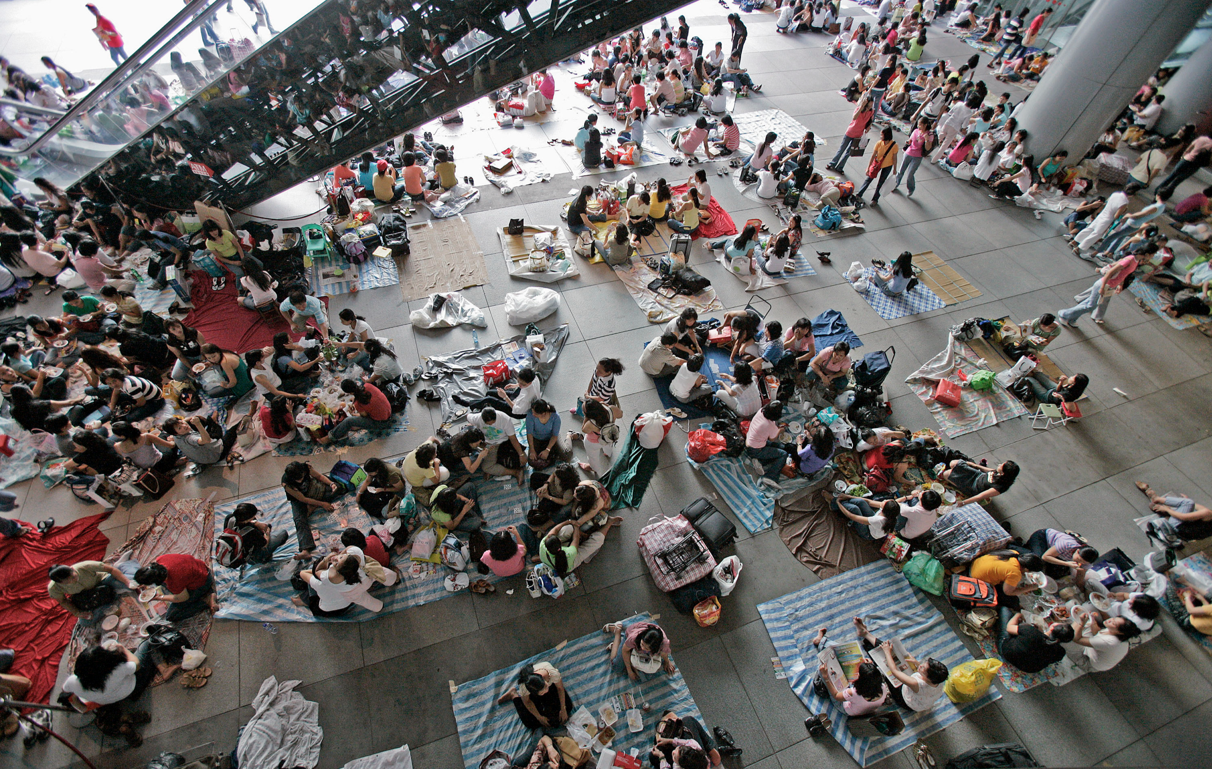 Foreign Helpers: an overhead view of people gathered on cardboard beneath a covered walkway.