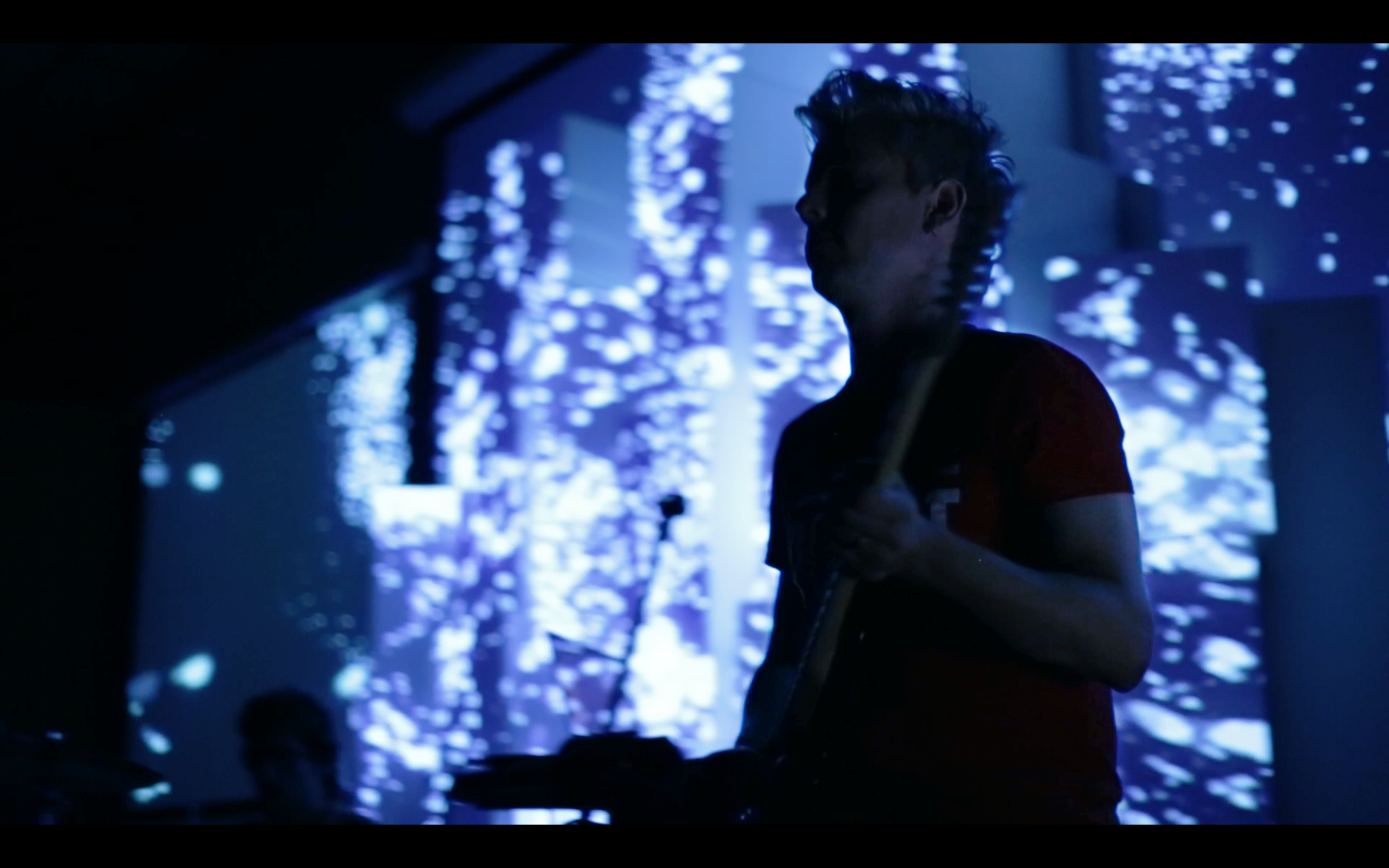 A guitarist performing in front of a blue pixelated projection at Lituania Lituania.
