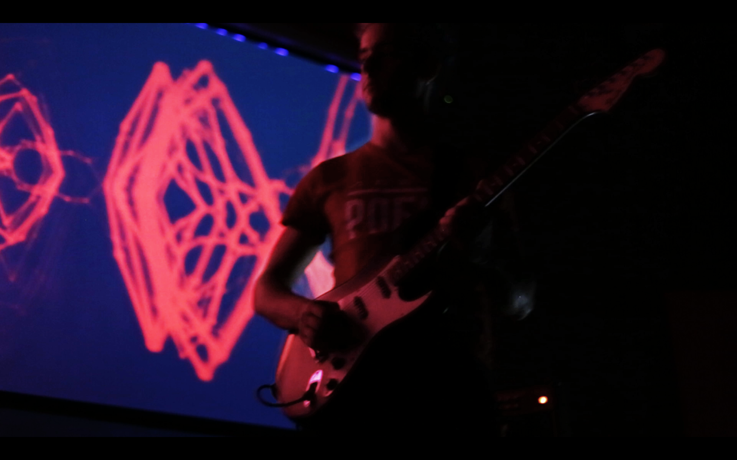 Close-up of a guitarist beneath a red geometric projection.