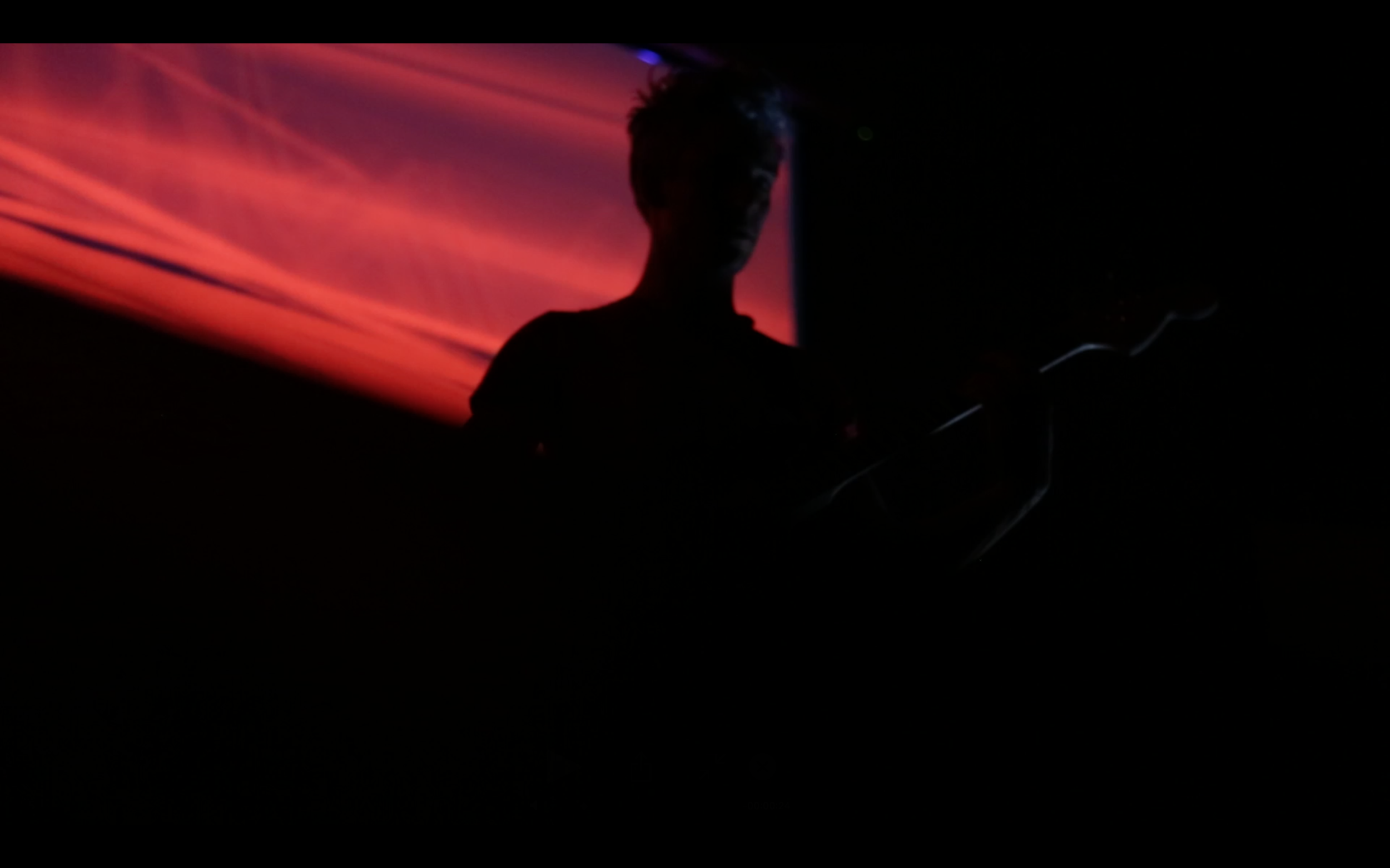 A guitarist silhouetted against a red and orange projection.