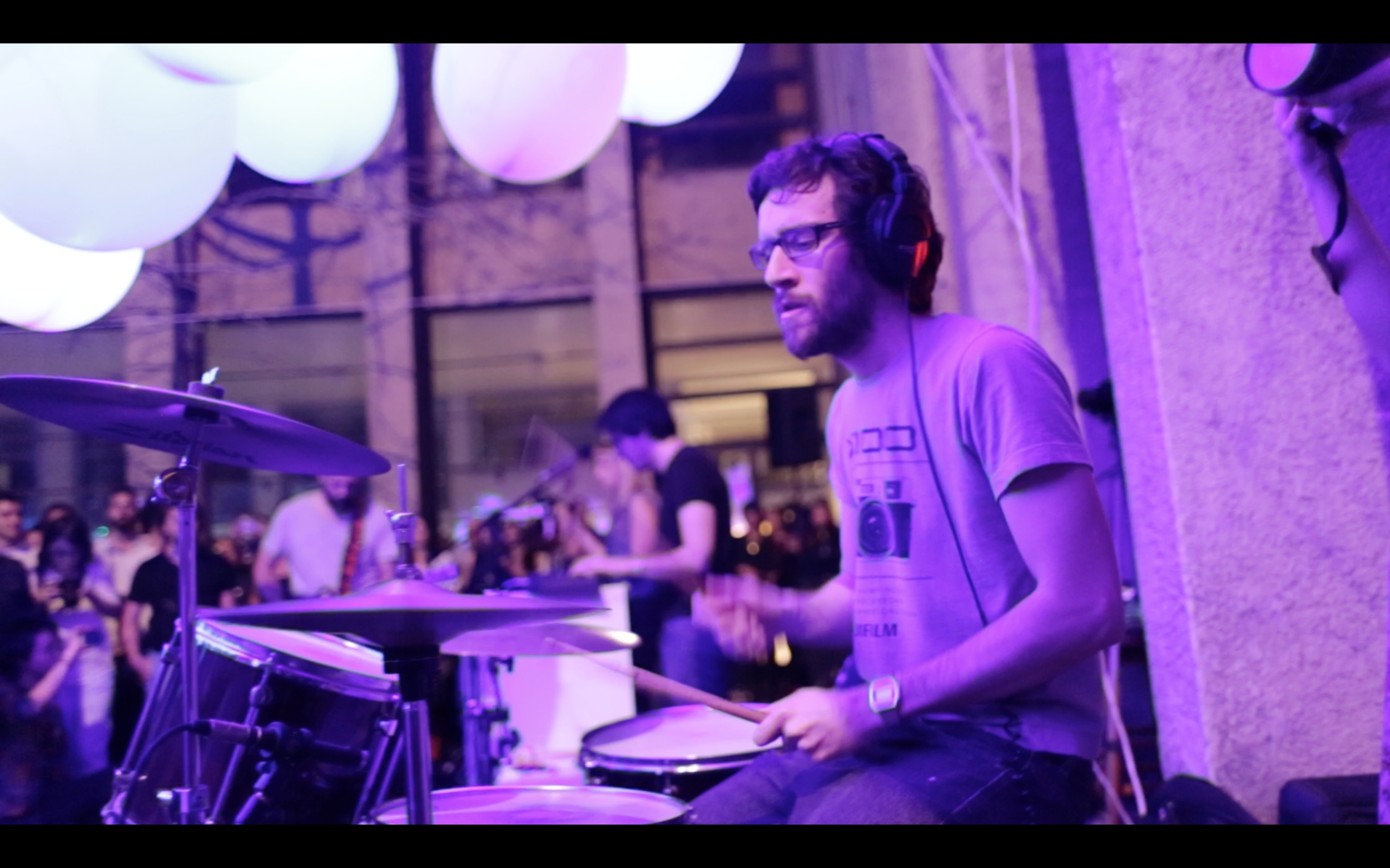 A drummer wearing headphones beneath purple balloons.
