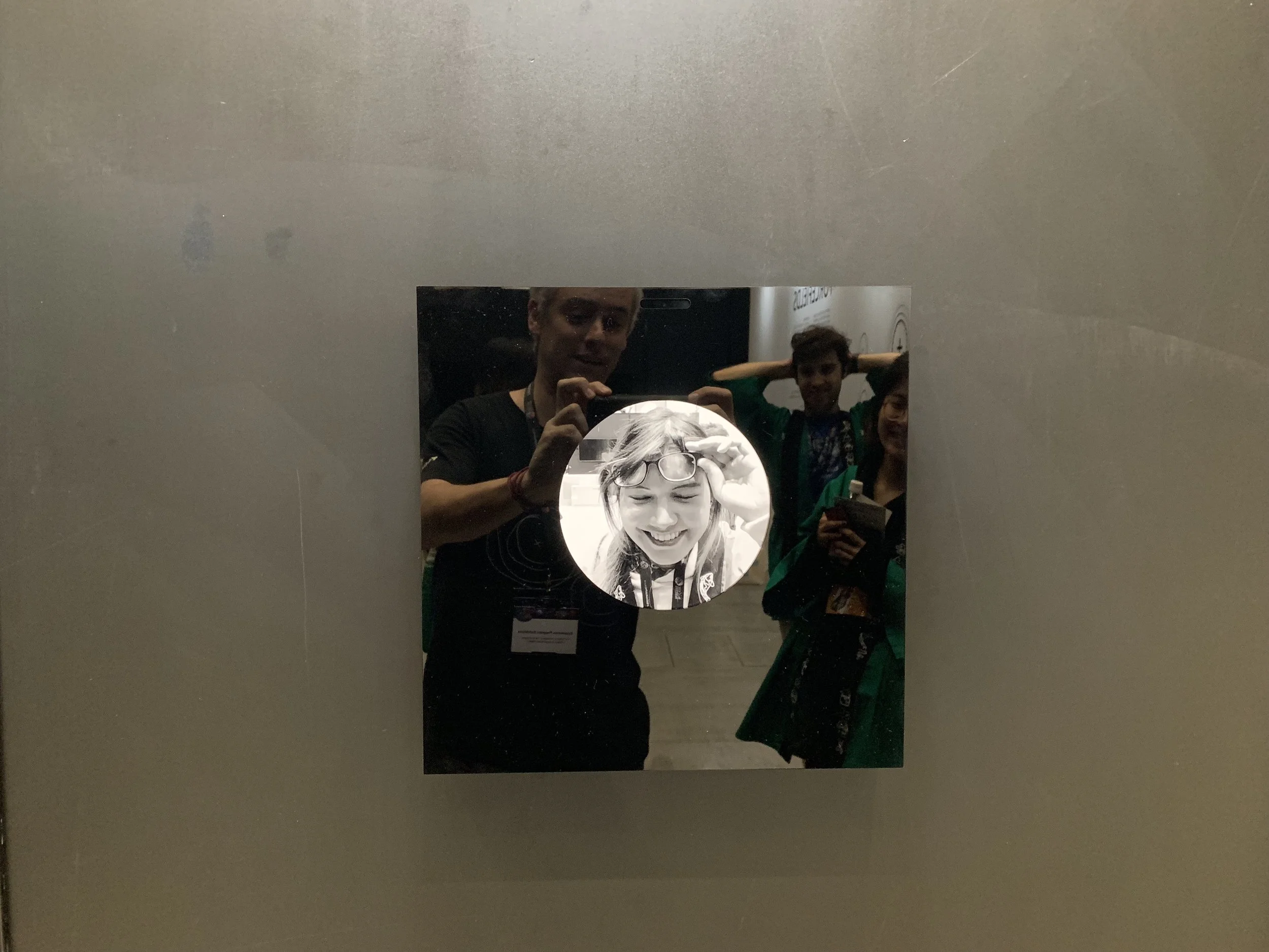 The glossy display reflects visitors around a circular closed-eye portrait.