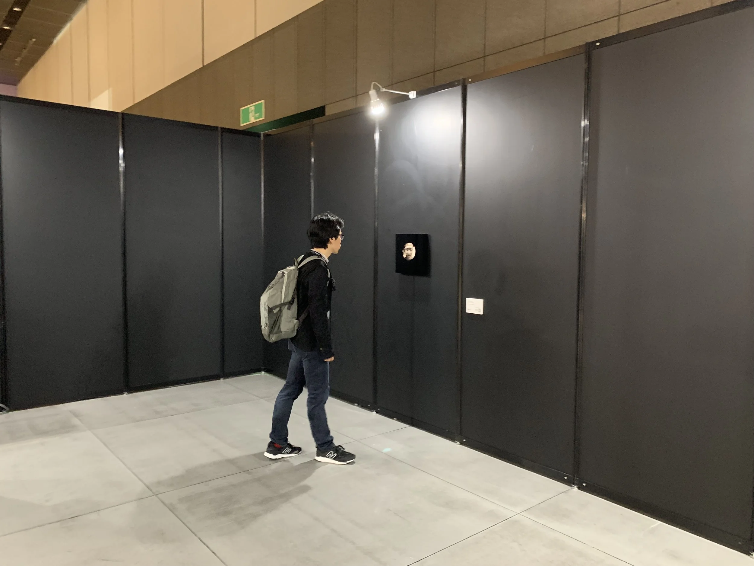 A visitor with a backpack approaches the portrait display in a dark-walled gallery.