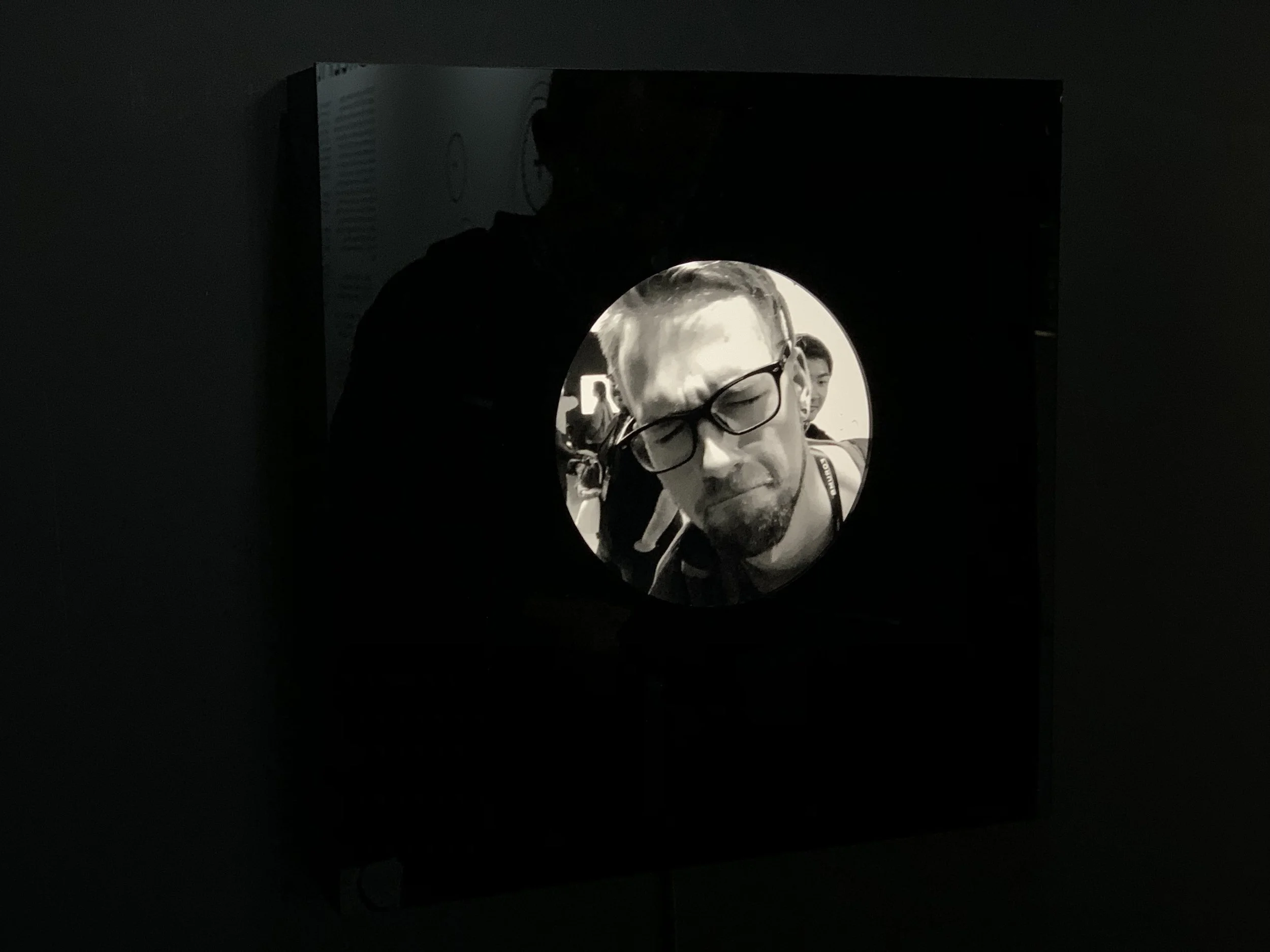 A close-up portrait wearing glasses appears in the circular display.