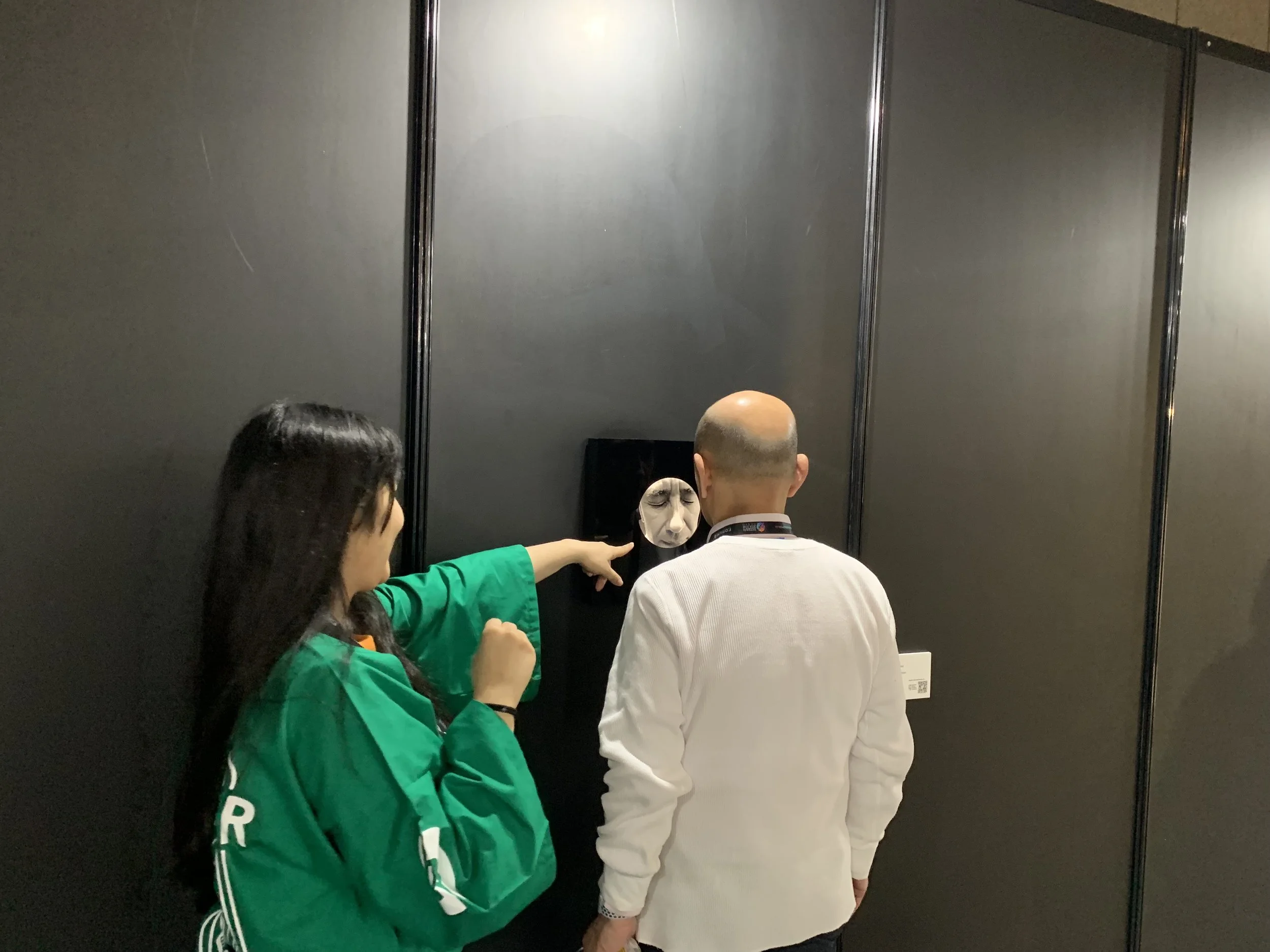 Two visitors face the portrait display in a darkened exhibition space.