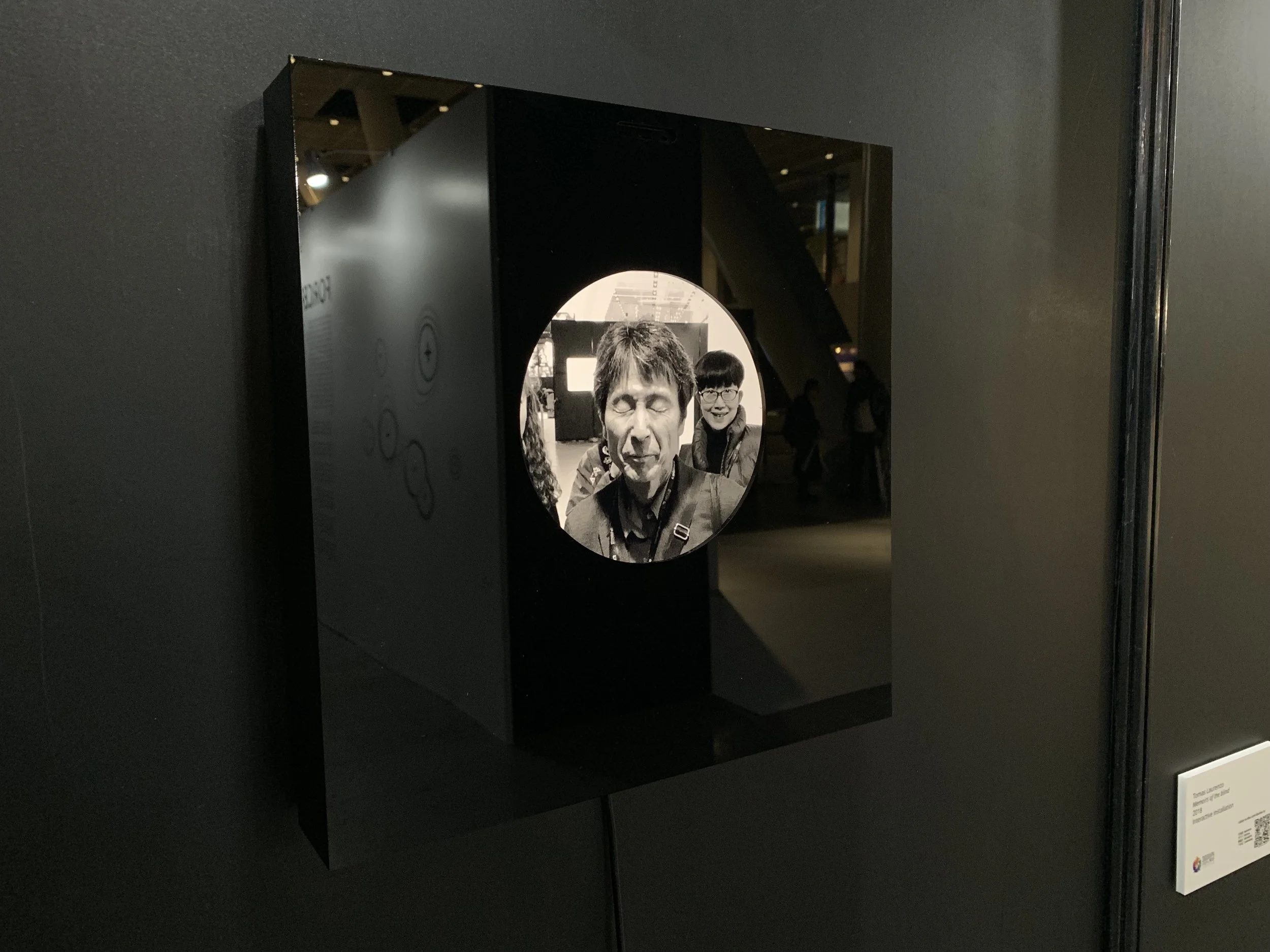 An angled view of the display with a closed-eye portrait and reflected gallery lights.