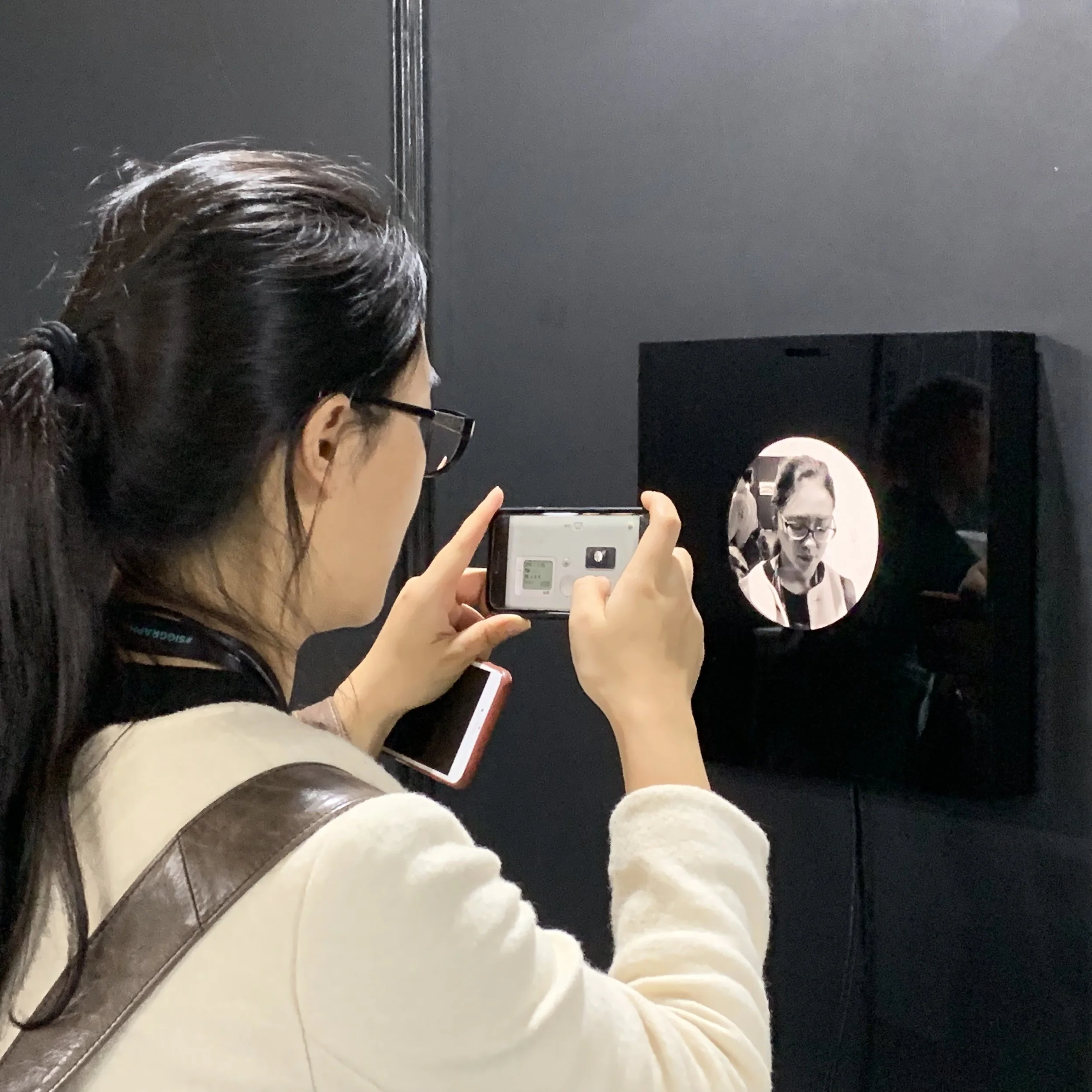 A visitor with glasses photographs the installation using a phone.
