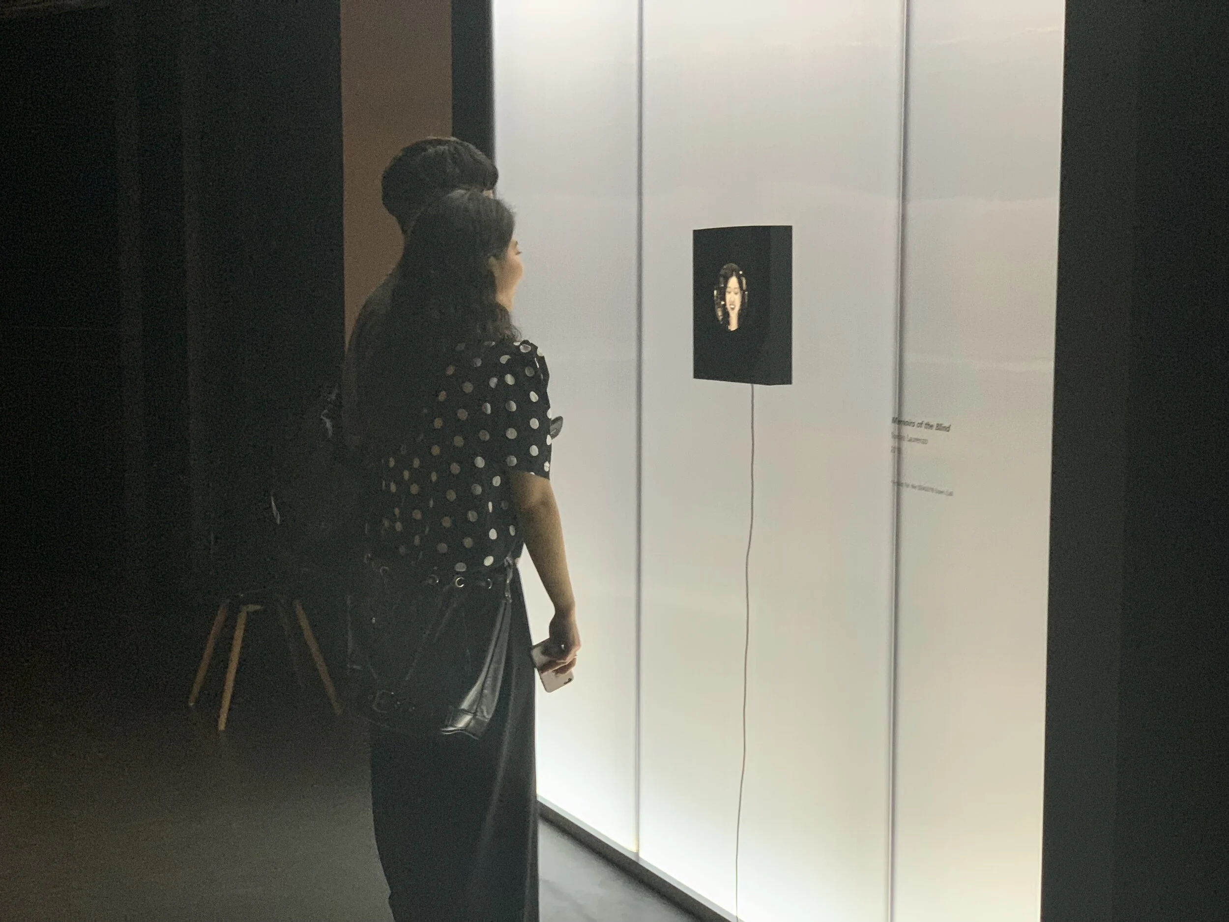 Two visitors face the small portrait display in the gallery.