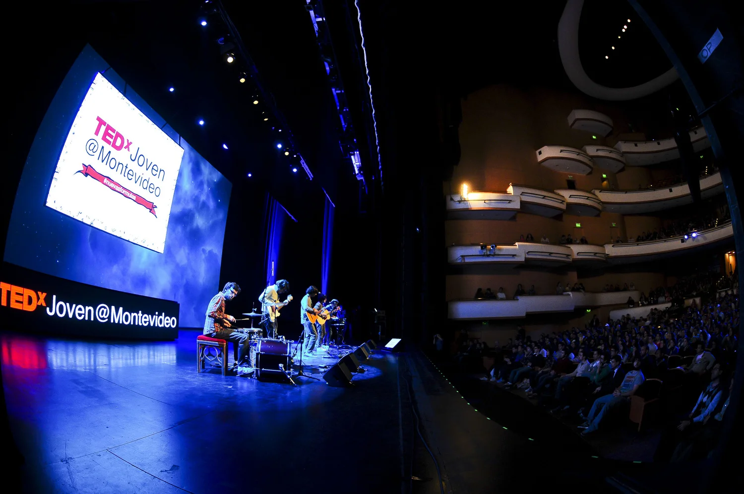 Musicians perform on the TEDx Montevideo stage with projected event graphics behind them.