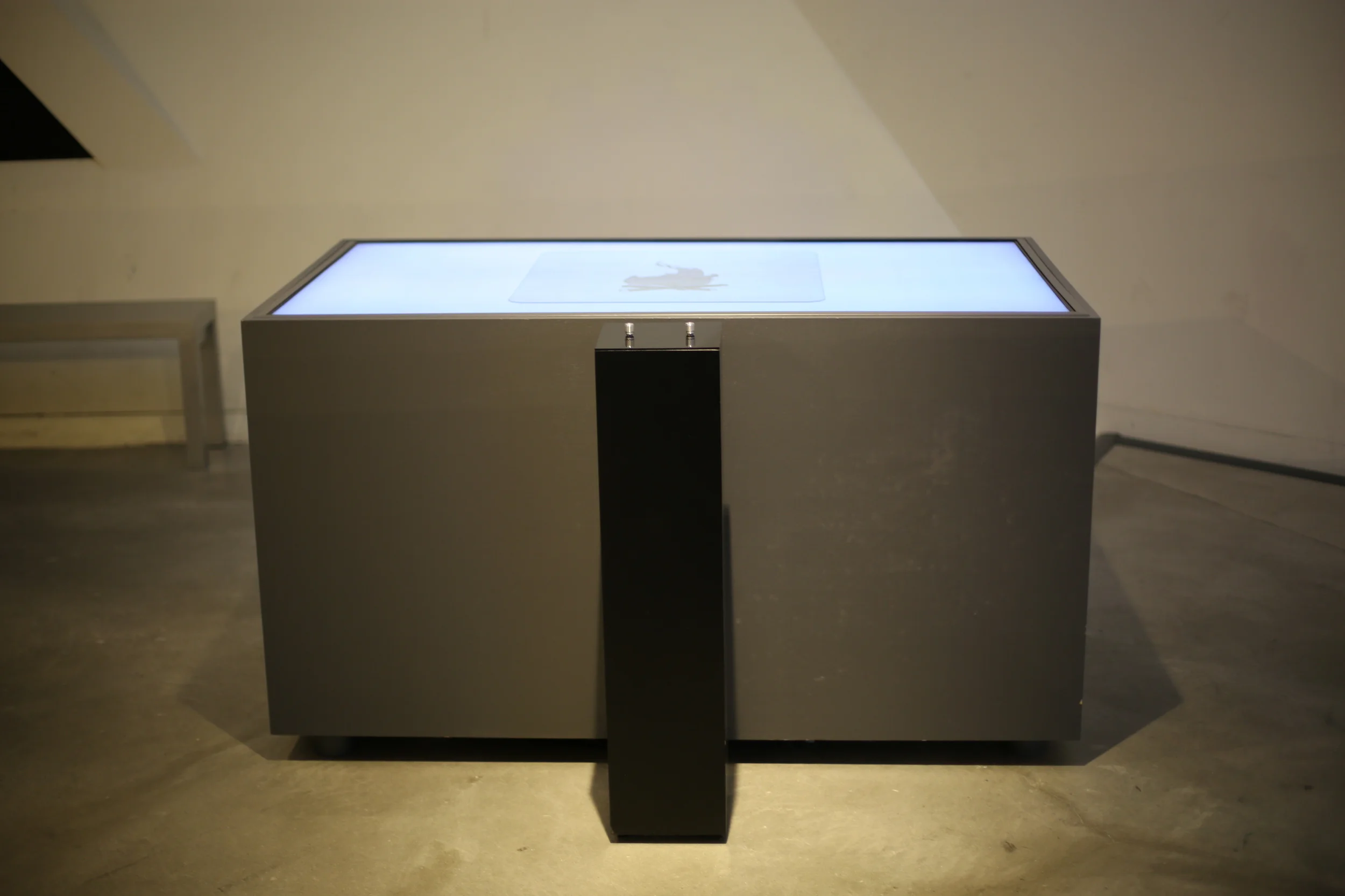 The white illuminated tabletop above the grey enclosure and black pedestal.