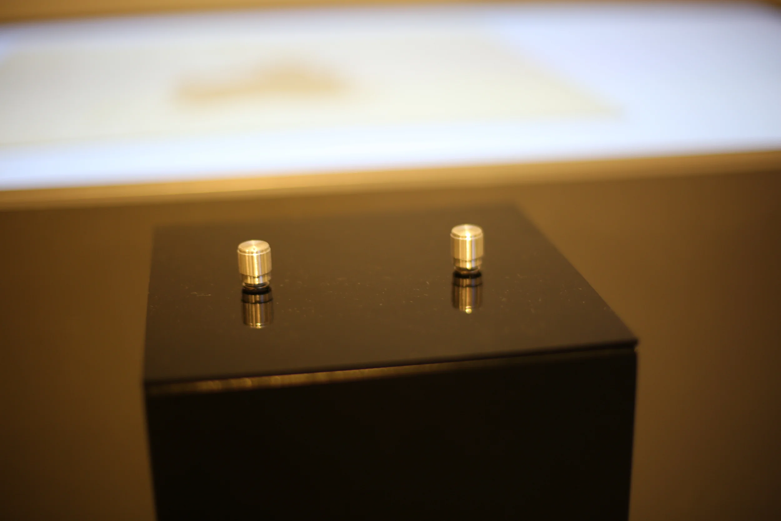 Two metallic controls on the black pedestal, with the tabletop blurred behind.