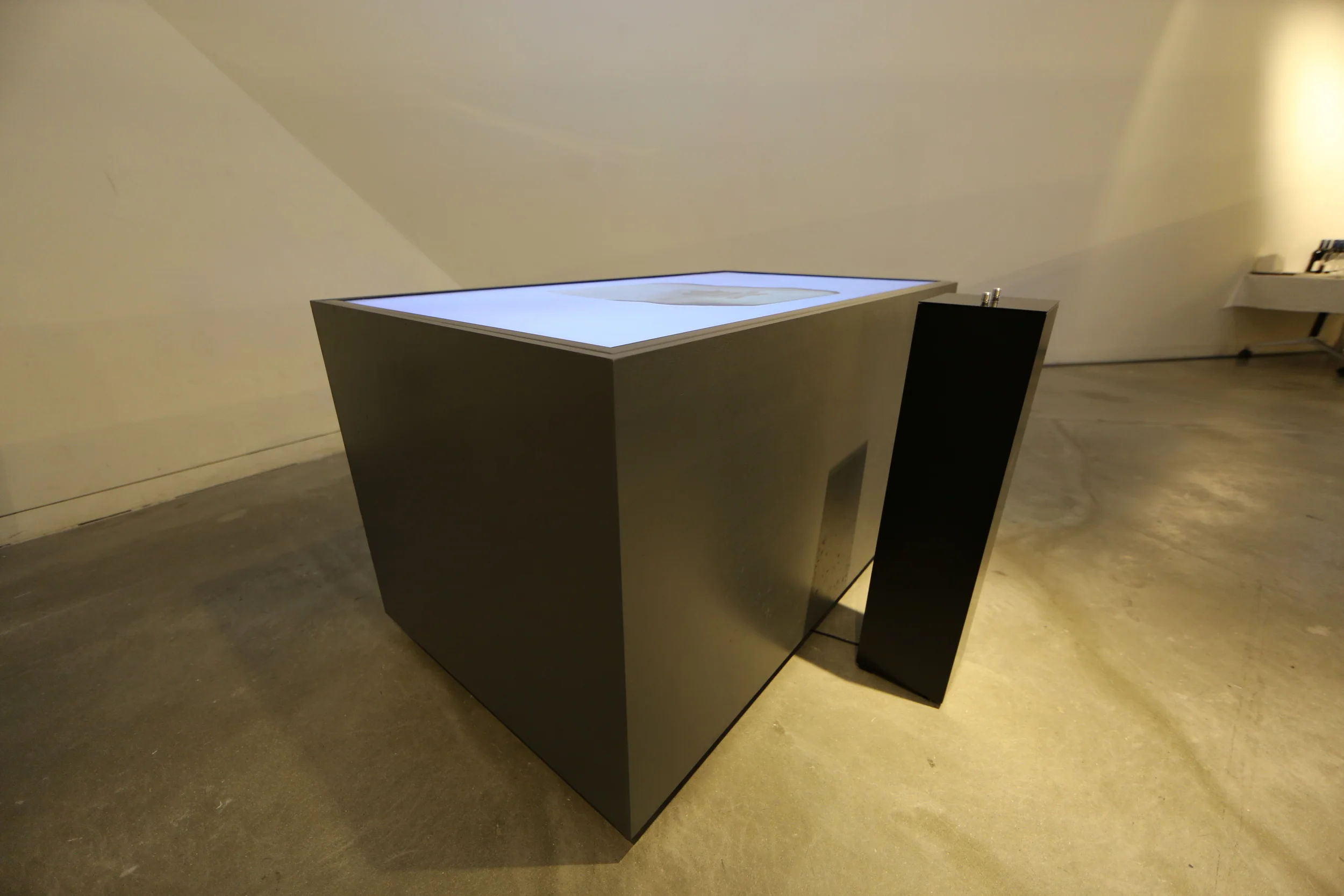 The side of the grey table enclosure beside the black control pedestal.