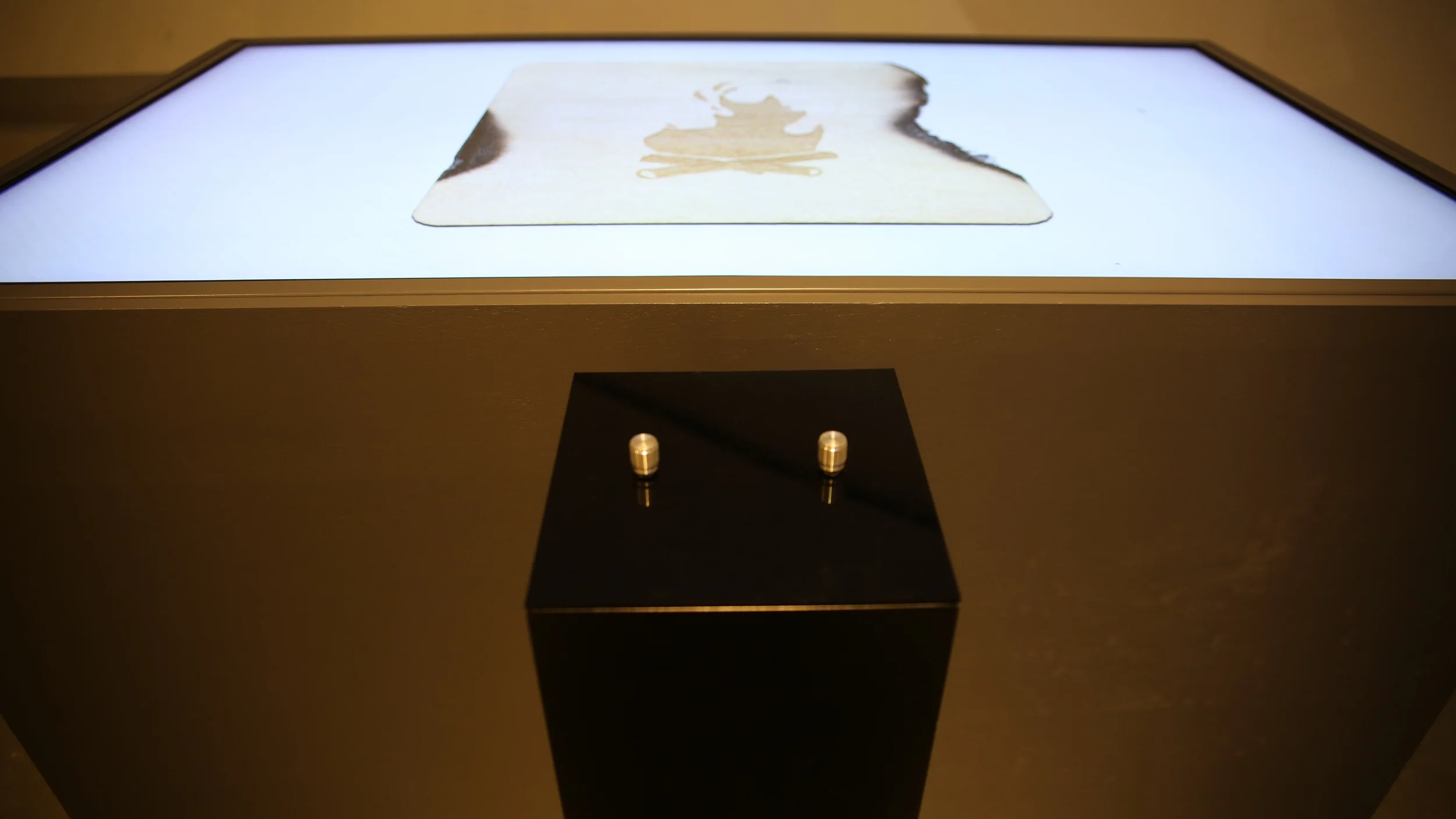 The control pedestal directly beneath the illuminated parchment image.